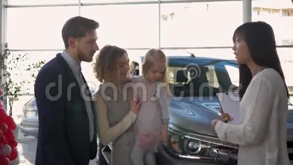 汽车购买年轻夫妇与小女孩建议与汽车销售商购买家庭车辆在销售中心视频的预览图