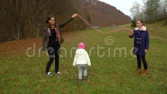 年轻的母亲在秋林里和孩子们玩耍小美女跳绳一家人很幸福视频的预览图
