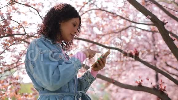 春天多种族的女人在公园里听音乐视频的预览图