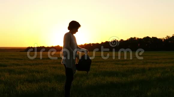 一个女孩穿着背包在夕阳的背景下沿着一片绿色的草坪动作缓慢视频的预览图