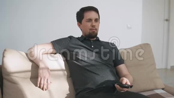 成年男子在电视前放松坐在沙发上换频道视频的预览图