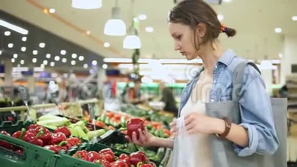 购物在蔬菜商店或超市选择生物红铃椒的女人一个接一个地把它放进视频的预览图
