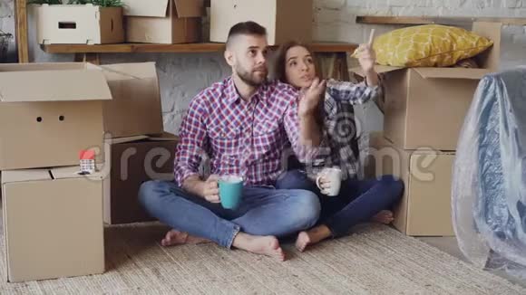幸福的一对夫妇坐在新房子的地板上谈论他们新房子的内部拿着杯子视频的预览图