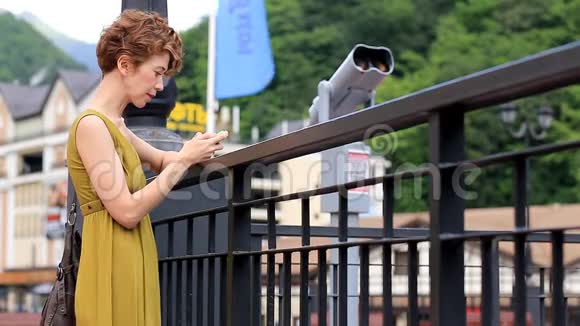夏天年轻可爱的女人站在街上在城市背景下的智能手机上输入一条信息视频的预览图