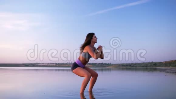 站在水中做仰卧起坐的年轻长头发的女人的侧视快乐健康的生活方式视频的预览图