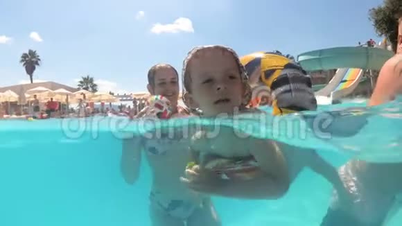 阳光明媚的一天小男孩在游泳池里用充气环游泳水下慢动作镜头视频的预览图