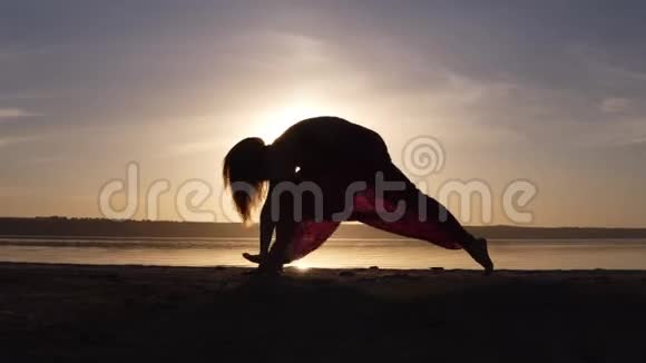 年轻女子在海滩上做劈腿瑜伽姿势运动员的美丽轮廓日落视频的预览图