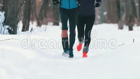 穿着运动服的男女青年在冬季森林里慢跑架子上的腿视频的预览图
