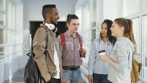 在大学里四个多民族的学生站在宽敞明亮的玻璃大厅里积极地交谈视频的预览图