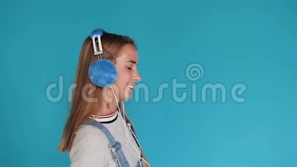 肖像可爱的女孩跳舞和移动的节奏听音乐耳机蓝色背景少女视频的预览图