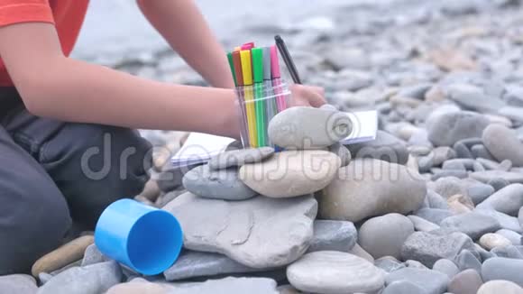 特写小男孩坐在海边的石滩上手里拿着记号笔作画视频的预览图