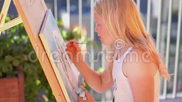 美丽的金发少女在露台上画一幅画视频的预览图