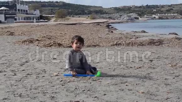 可爱的幼儿坐在沙滩上玩塑料高尔夫球棒和沙滩视频的预览图
