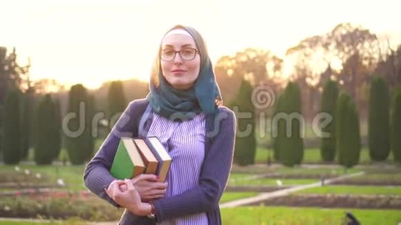 肖像穆斯林学生戴着头巾背着背包在日落公园里读书视频的预览图