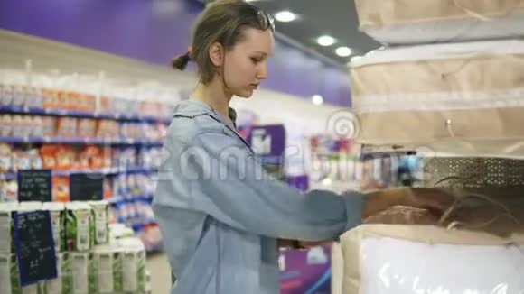 一个穿牛仔衬衫的年轻女孩在超市里挑选产品外观和触摸枕头的质量或视频的预览图
