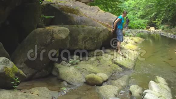 徒步旅行美丽的女人带着背包用智能手机在山河上拍照大石头和绿色的苔藓视频的预览图