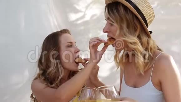 两个女人的背景上有白色的床单漂亮的女孩用牛角面包互相喂食夏季视频的预览图