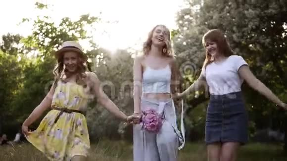 女人的友谊三个穿夏季服装的漂亮女孩牵着手在森林里嬉戏地散步视频的预览图