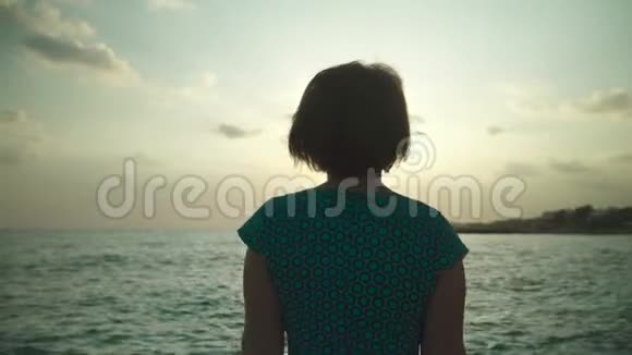 穿着绿色短裙的女人在潮湿的岩石上散步阳光下溅起海水日落时分视频的预览图