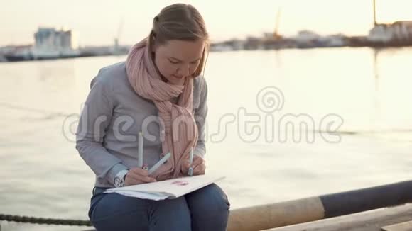 年轻女子在春天傍晚坐在码头附近用铅笔画画视频的预览图