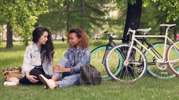 漂亮的非洲裔美国女人在公园里和她的欧洲朋友聊天坐在草地上女孩们在聊天视频的预览图