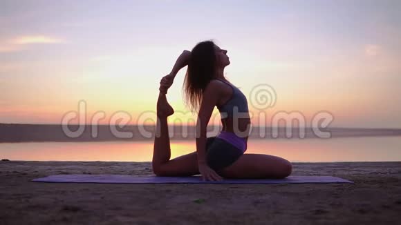 迷人的瑜伽女人在海边的垫子上锻炼混合瑜伽姿势清晨黄昏视频的预览图