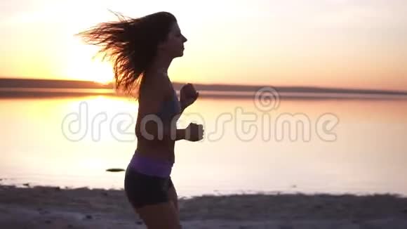 一个穿着运动服在海边或湖边奔跑的漂亮运动女孩侧视图视频的预览图