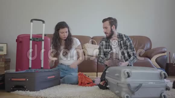 男人和女人坐在家里的地板上在皮革沙发前在旅行前收拾一个手提箱丈夫视频的预览图