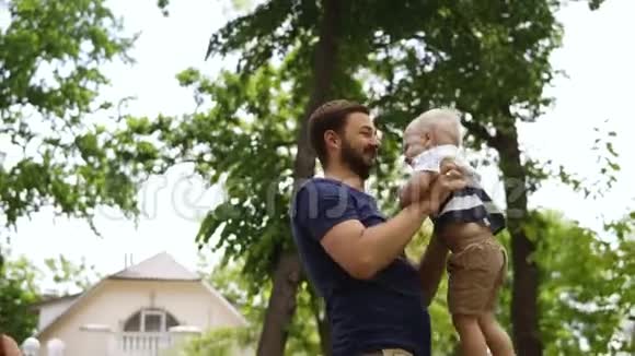 年轻的父亲穿着休闲服装留着胡子抱着他的金发小儿子孩子光着脚他亲儿子视频的预览图