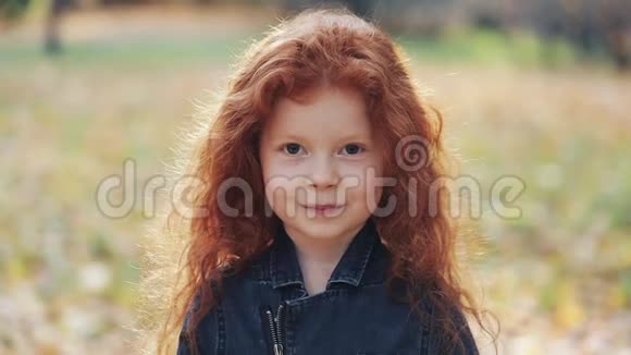 可爱的小红发女孩微笑的肖像隐藏了她的眼睛黄叶可爱的孩子躲在黄色的叶子上秋天视频的预览图