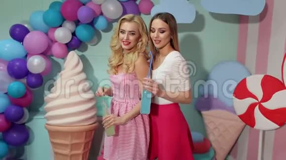 两个穿着鲜艳夏装的女孩喝果汁或玻璃瓶中的鸡尾酒视频的预览图