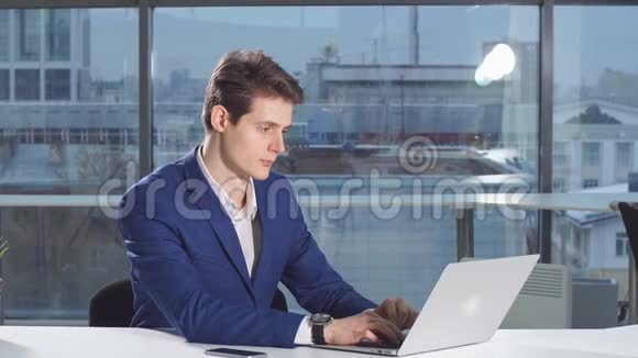 年轻的现代商人用手提电脑在办公桌上工作视频的预览图