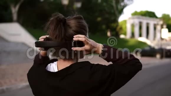 一个年轻的现代女孩在公园或街道上随意散步的背面景色回头看她的肩膀视频的预览图