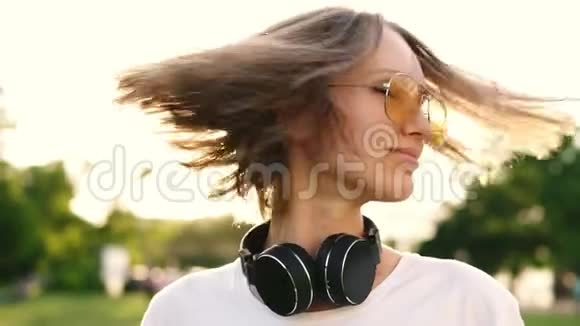 年轻漂亮的女孩留着短发在绿色公园的背景下摇头穿黄色衣服的白人女人视频的预览图