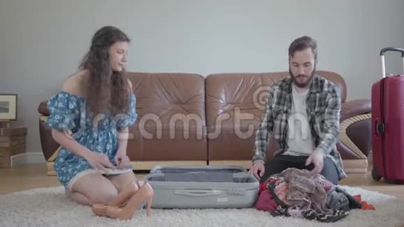 男人和女人坐在家里的地板上前面有一个皮革沙发旅行前收拾一个手提箱丈夫视频的预览图
