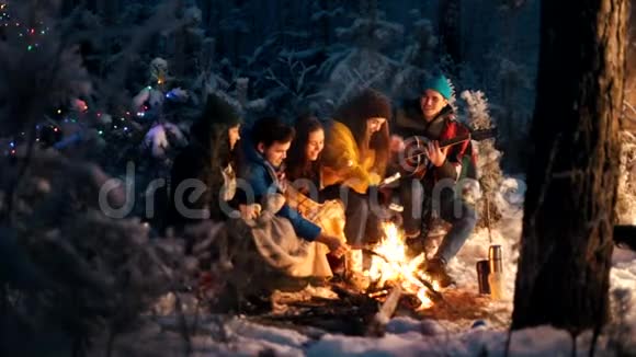 一群朋友坐在冬天的森林里吃着棉花糖一个拿着吉他的年轻人视频的预览图