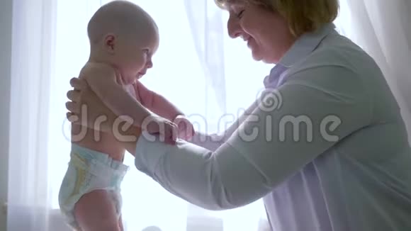 在背光窗口附近的按摩台上医生帮助婴儿制作步骤视频的预览图