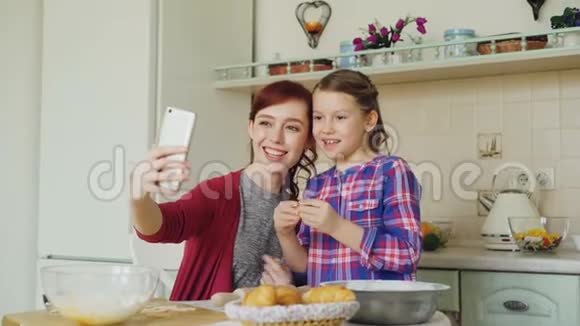 微笑的妈妈和有趣的女儿一起用智能手机相机自拍在做饭的时候做傻脸视频的预览图