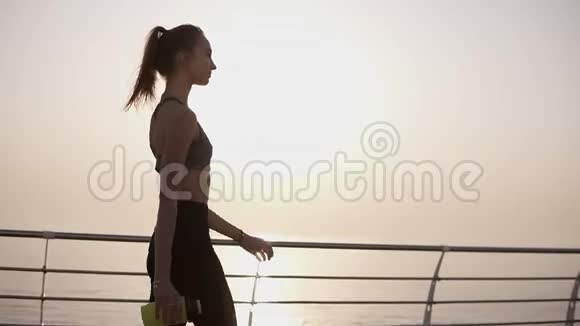华丽的侧景一个美丽的女孩走在沿着大海的道路上阳光静静地照耀着一个穿黑色紧身裤的女孩视频的预览图