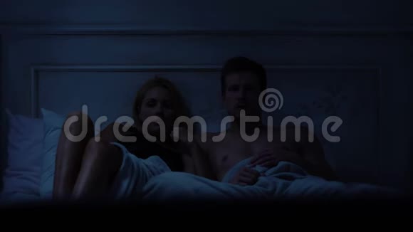 恐惧的夫妻看恐怖电影坐在床上周末休闲视频的预览图