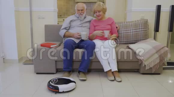 家中的老人在沙发上放松用机器人吸尘器清洁地板视频的预览图