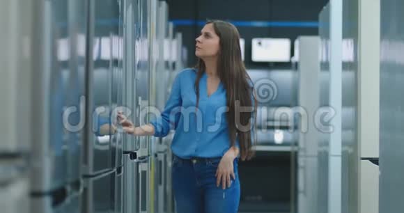 一位年轻的女士打开冰箱门存放电器并与其他模特比较购买新房子视频的预览图