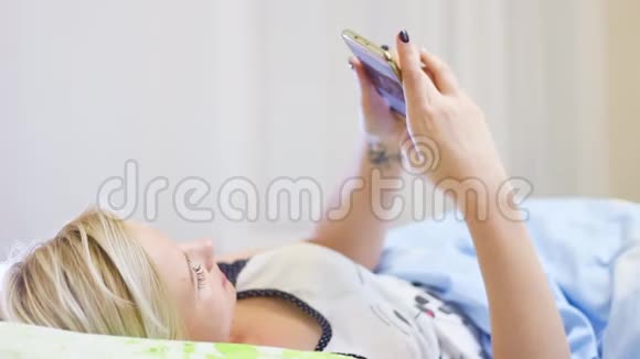 美丽的金发女孩躺在床上用电话视频的预览图