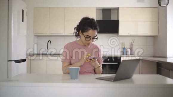 厨房里用笔记本电脑和电话的年轻女子视频的预览图