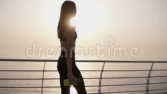 一个漂亮优雅的女孩穿着运动服走在长廊上手里拿着运动瓶斯利姆阳光明媚慢慢视频的预览图