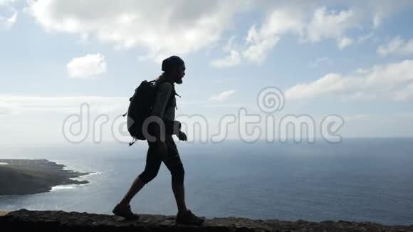 带背垫的男性徒步旅行者正走在大洋上方加那利群岛的一条路的边缘视频的预览图