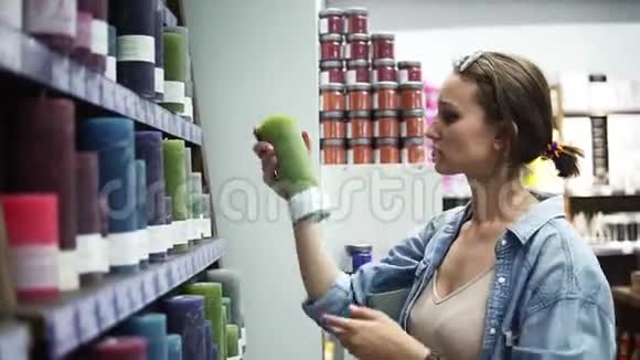 从超市里的架子上挑选不同颜色的蜡烛的有吸引力的女人的侧面视图闻到绿烛的味道视频的预览图