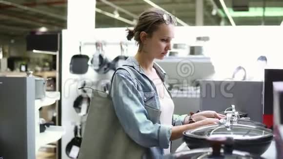 一位年轻女子穿着牛仔衬衫购物的录像找厨房的东西检查各种锅碗瓢盆视频的预览图