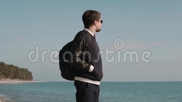 大胡子的年轻人站在海边在阳光明媚的日子里欣赏风景视频的预览图