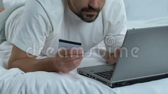 男性在床上输入笔记本电脑应用程序网上银行购物卡号码视频的预览图